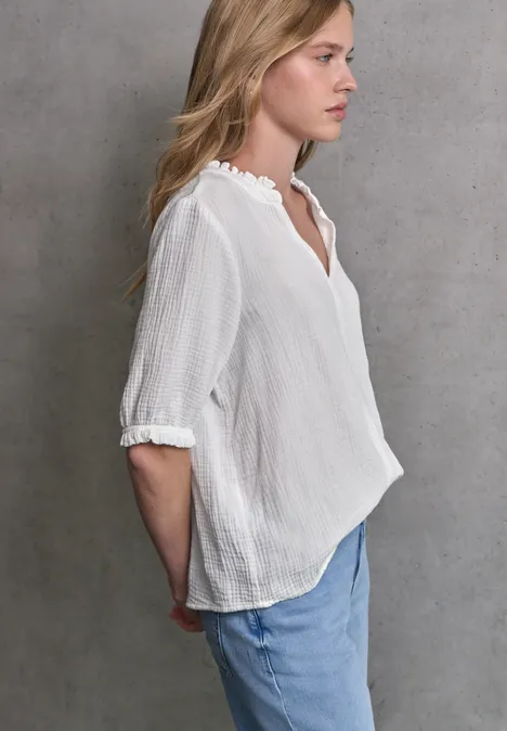 Frau mit weißer Bluse und heller Jeans, schaut leicht zur Seite.